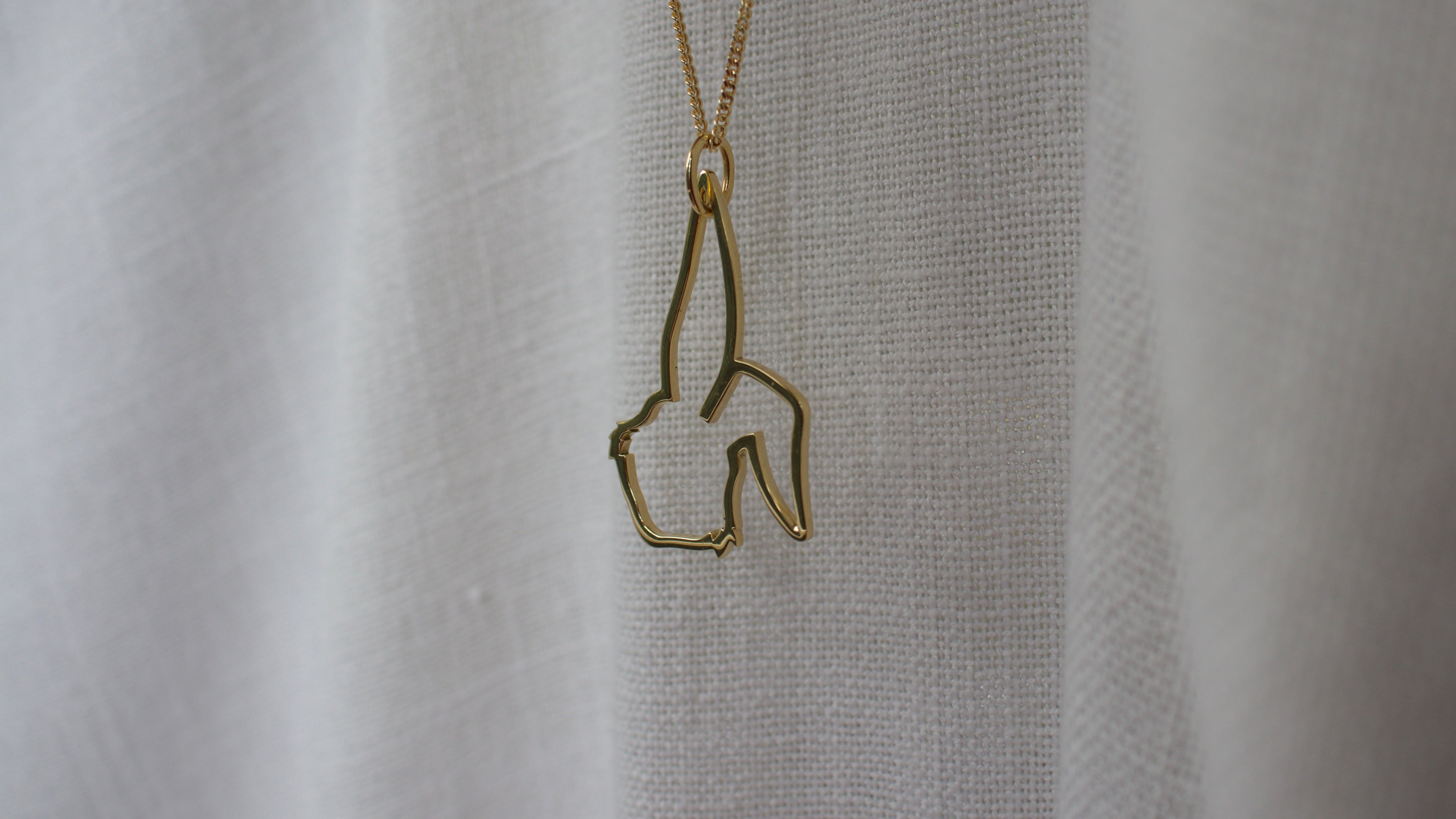 Gold necklace with a unique pendant on a textured beige background